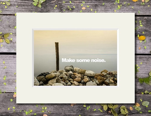 A quiet waterside scene with Make Some Noise'' quote