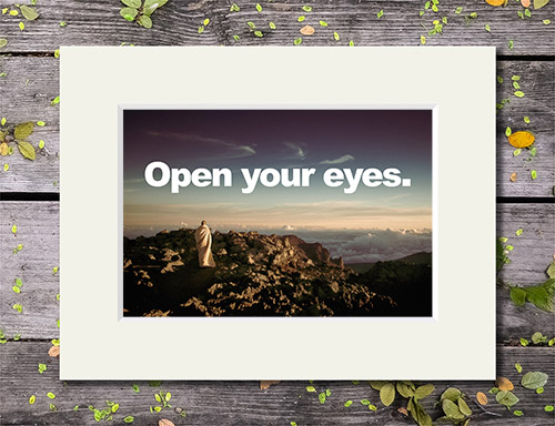 Lone figure in white on a mountain top with 'Open Your Eyes' quote